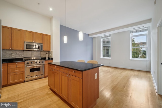 kitchen with hanging light fixtures, light hardwood / wood-style flooring, appliances with stainless steel finishes, tasteful backsplash, and a kitchen island