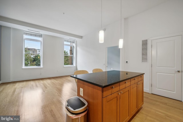 kitchen featuring dark stone countertops, a kitchen island, hanging light fixtures, and light wood-type flooring