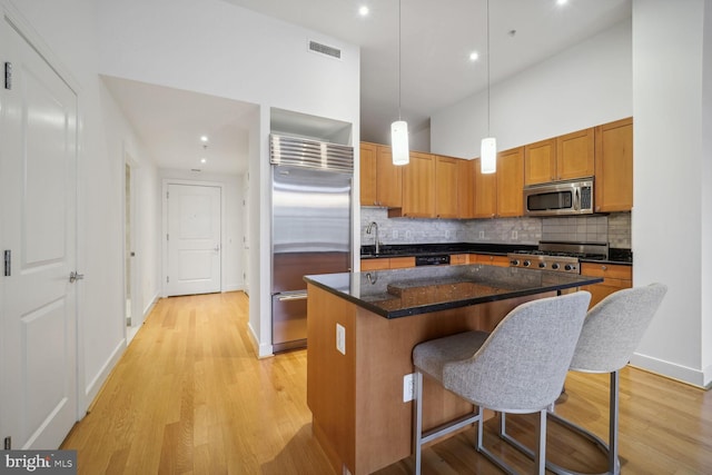 kitchen with appliances with stainless steel finishes, high vaulted ceiling, light hardwood / wood-style floors, a kitchen island, and hanging light fixtures