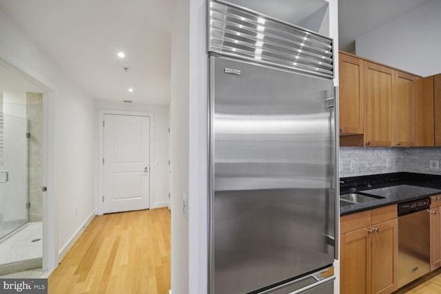 kitchen featuring backsplash, dark stone counters, stainless steel appliances, sink, and light hardwood / wood-style flooring