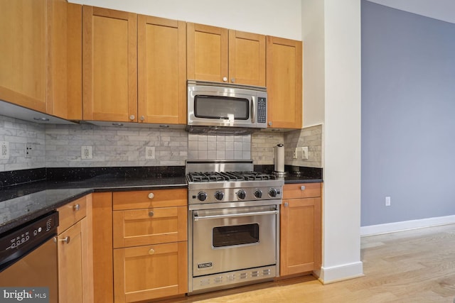 kitchen featuring dark stone countertops, light wood-type flooring, backsplash, and appliances with stainless steel finishes