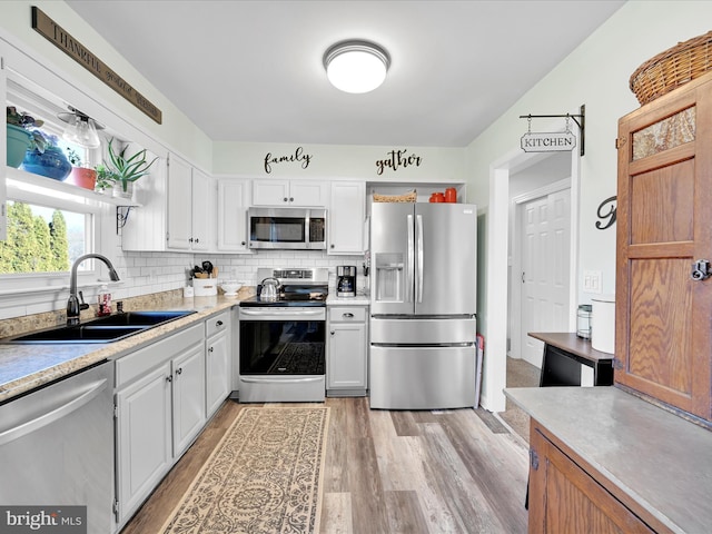 kitchen with light wood-type flooring, tasteful backsplash, stainless steel appliances, sink, and white cabinets