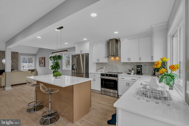 kitchen with a center island, wall chimney range hood, decorative backsplash, white cabinets, and appliances with stainless steel finishes