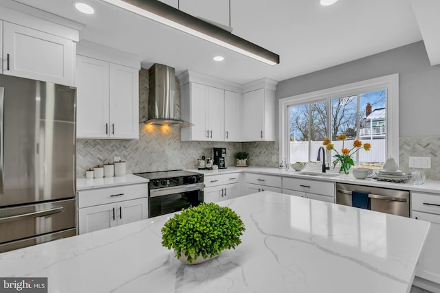 kitchen featuring light stone counters, sink, stainless steel appliances, and wall chimney range hood