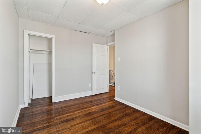 unfurnished bedroom with a paneled ceiling, a closet, and dark hardwood / wood-style flooring