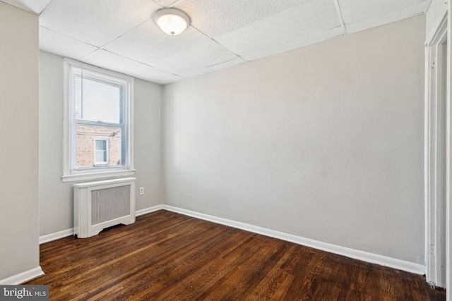 spare room with dark hardwood / wood-style flooring, radiator heating unit, and a drop ceiling