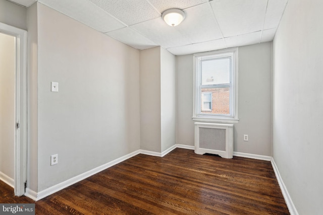 unfurnished room with a paneled ceiling, dark wood-type flooring, and radiator