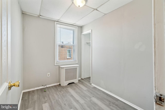 empty room with radiator heating unit, a paneled ceiling, and light hardwood / wood-style floors