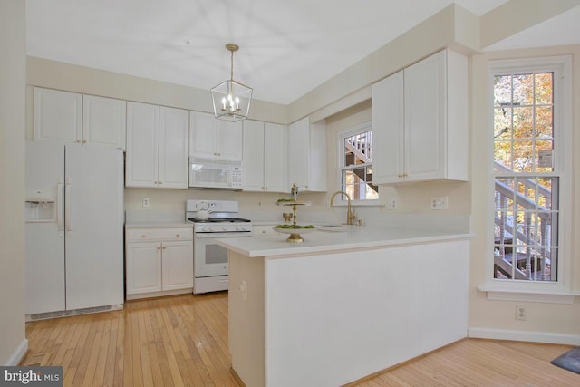 kitchen featuring white appliances, hanging light fixtures, light hardwood / wood-style flooring, white cabinetry, and kitchen peninsula