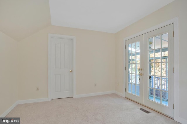 carpeted spare room featuring french doors and vaulted ceiling