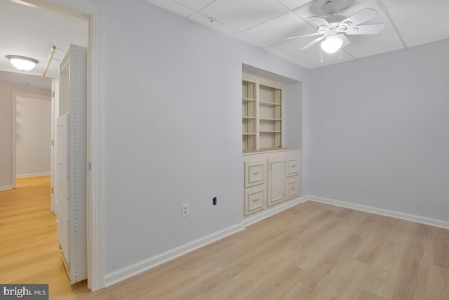 unfurnished room with a drop ceiling, ceiling fan, built in features, and light hardwood / wood-style flooring