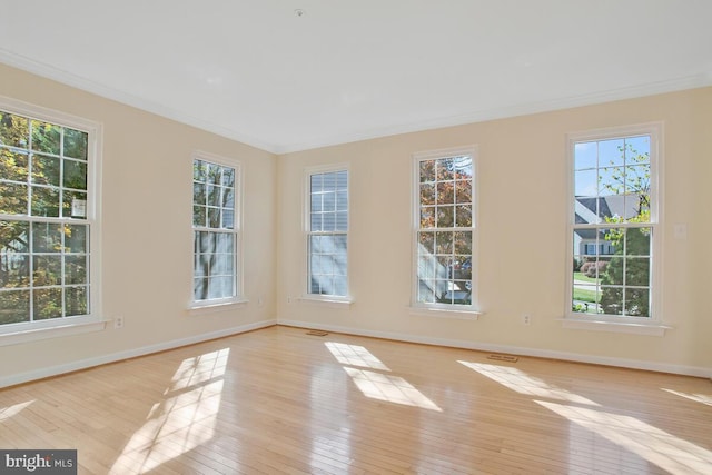 spare room with a healthy amount of sunlight, light wood-type flooring, and crown molding