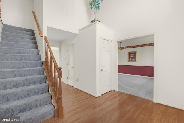 stairway featuring wood finished floors, a towering ceiling, and baseboards