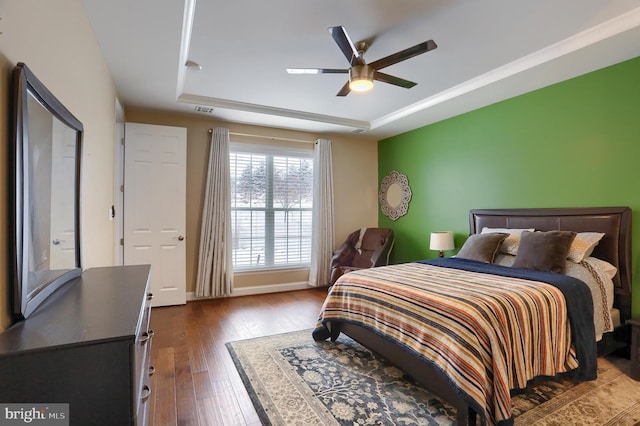 bedroom with a ceiling fan, visible vents, a tray ceiling, and dark wood-style flooring