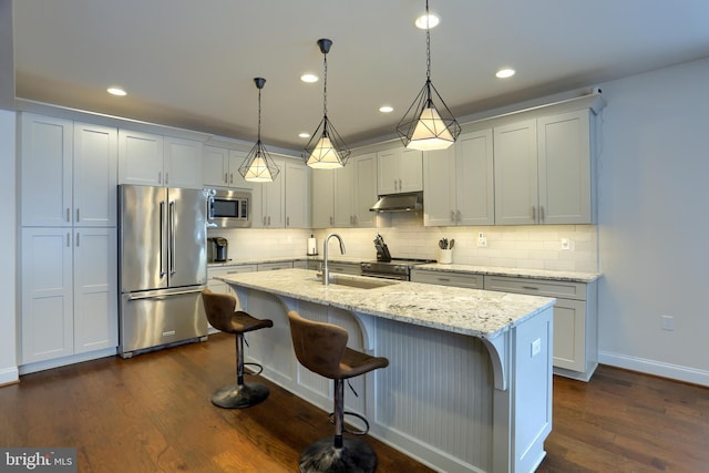 kitchen with pendant lighting, appliances with stainless steel finishes, sink, and a center island with sink