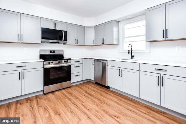 kitchen with gray cabinetry, sink, appliances with stainless steel finishes, and light hardwood / wood-style flooring