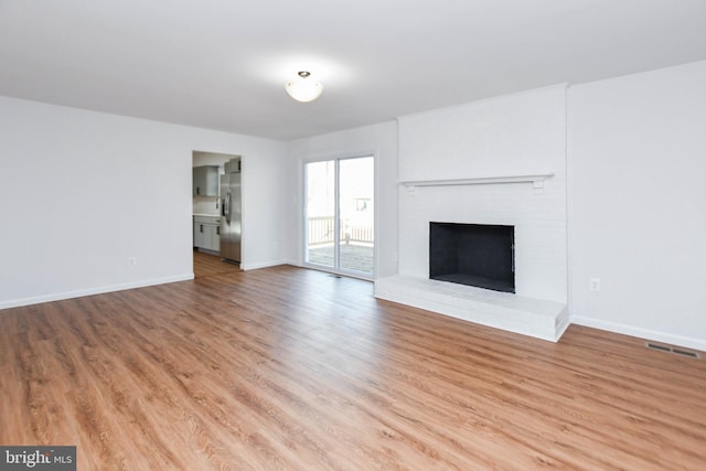 unfurnished living room with light hardwood / wood-style flooring and a brick fireplace