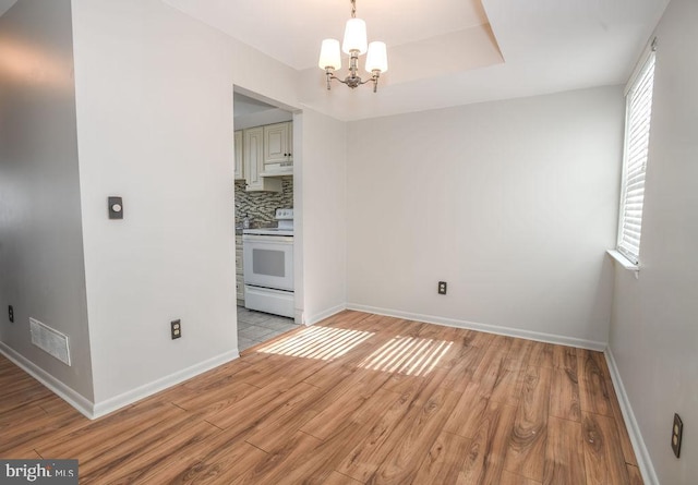 unfurnished dining area featuring a notable chandelier, a tray ceiling, and light wood-type flooring