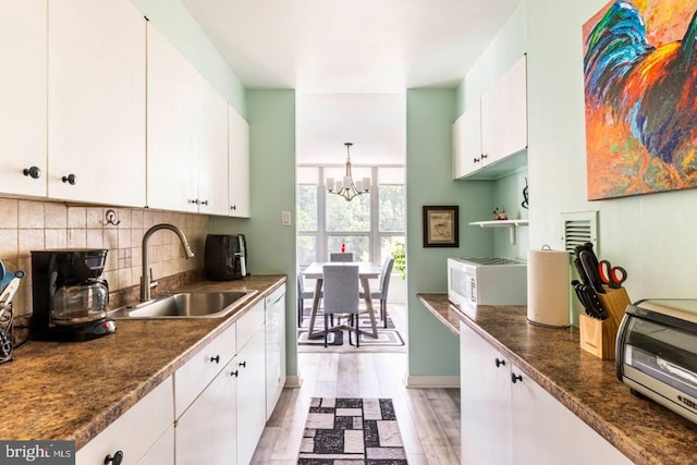 kitchen featuring white cabinetry, sink, light hardwood / wood-style flooring, a notable chandelier, and backsplash