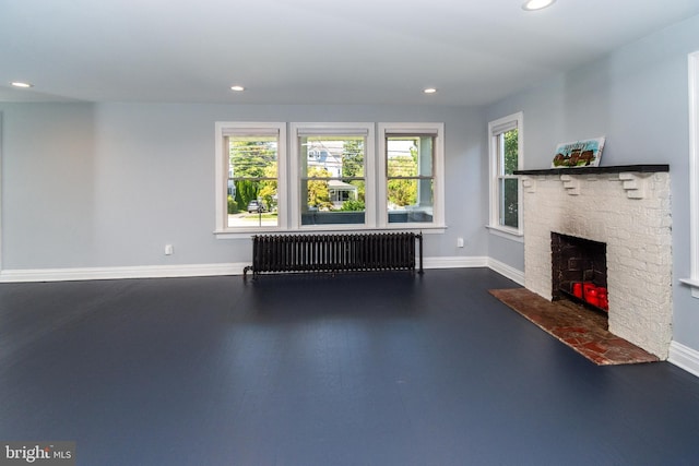 unfurnished living room featuring radiator, a healthy amount of sunlight, and a brick fireplace