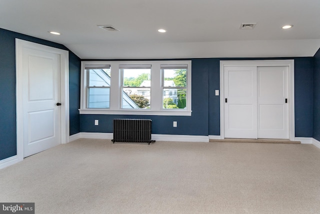 unfurnished bedroom featuring light colored carpet, radiator, and vaulted ceiling