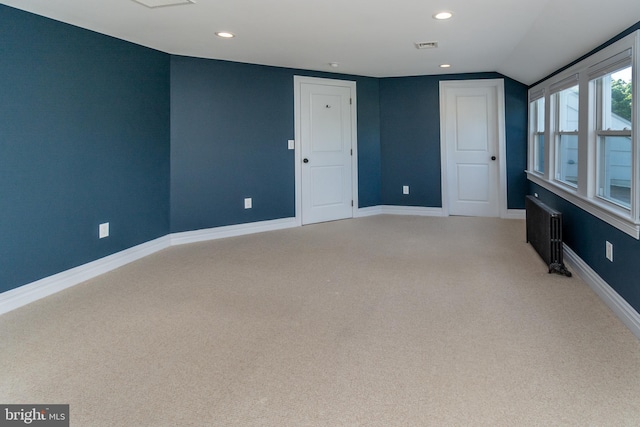 spare room with radiator heating unit, light colored carpet, and vaulted ceiling