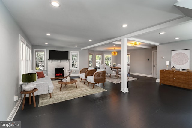 living room featuring dark wood-type flooring, a brick fireplace, and a notable chandelier