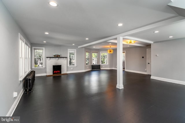 unfurnished living room featuring radiator, an inviting chandelier, dark hardwood / wood-style flooring, beamed ceiling, and a fireplace