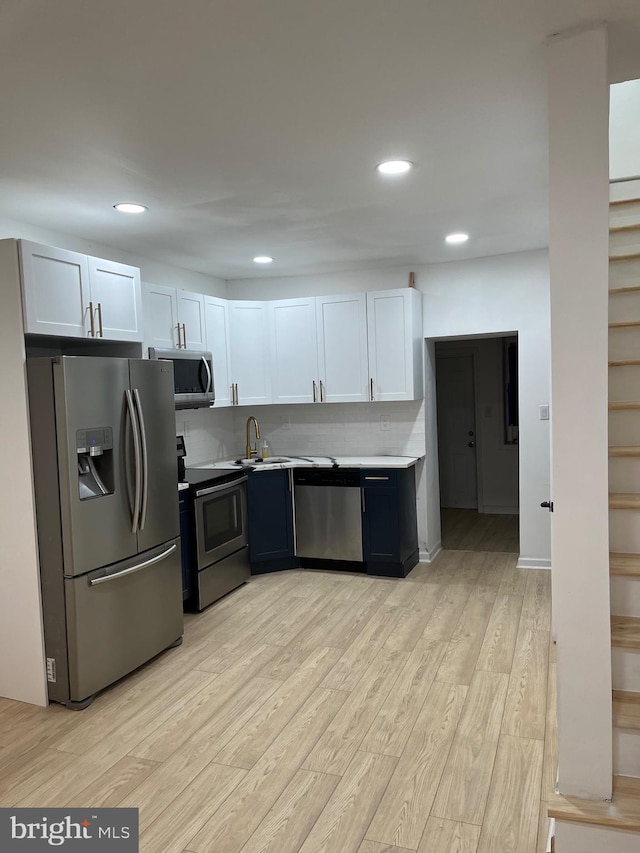 kitchen with sink, stainless steel appliances, tasteful backsplash, white cabinets, and light wood-type flooring