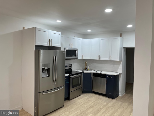 kitchen featuring appliances with stainless steel finishes, tasteful backsplash, white cabinetry, sink, and light wood-type flooring