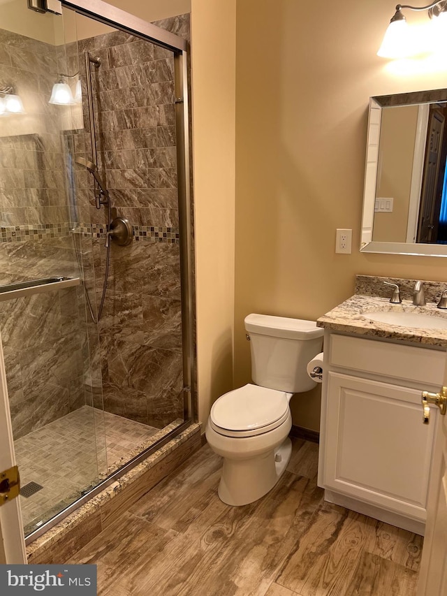 bathroom with hardwood / wood-style floors, vanity, toilet, and a shower with shower door