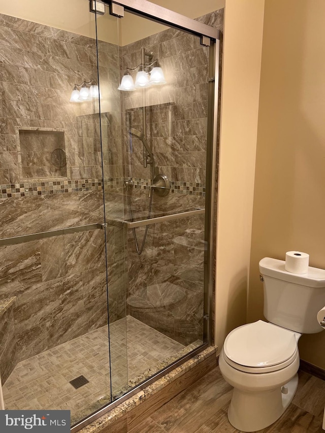 bathroom featuring hardwood / wood-style floors, a shower with shower door, and toilet