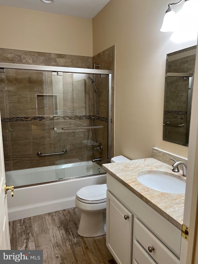 full bathroom featuring toilet, hardwood / wood-style floors, vanity, and combined bath / shower with glass door