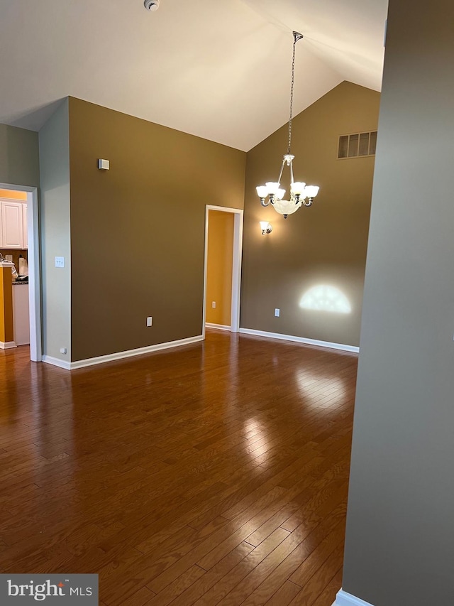 empty room with dark hardwood / wood-style floors, lofted ceiling, and an inviting chandelier