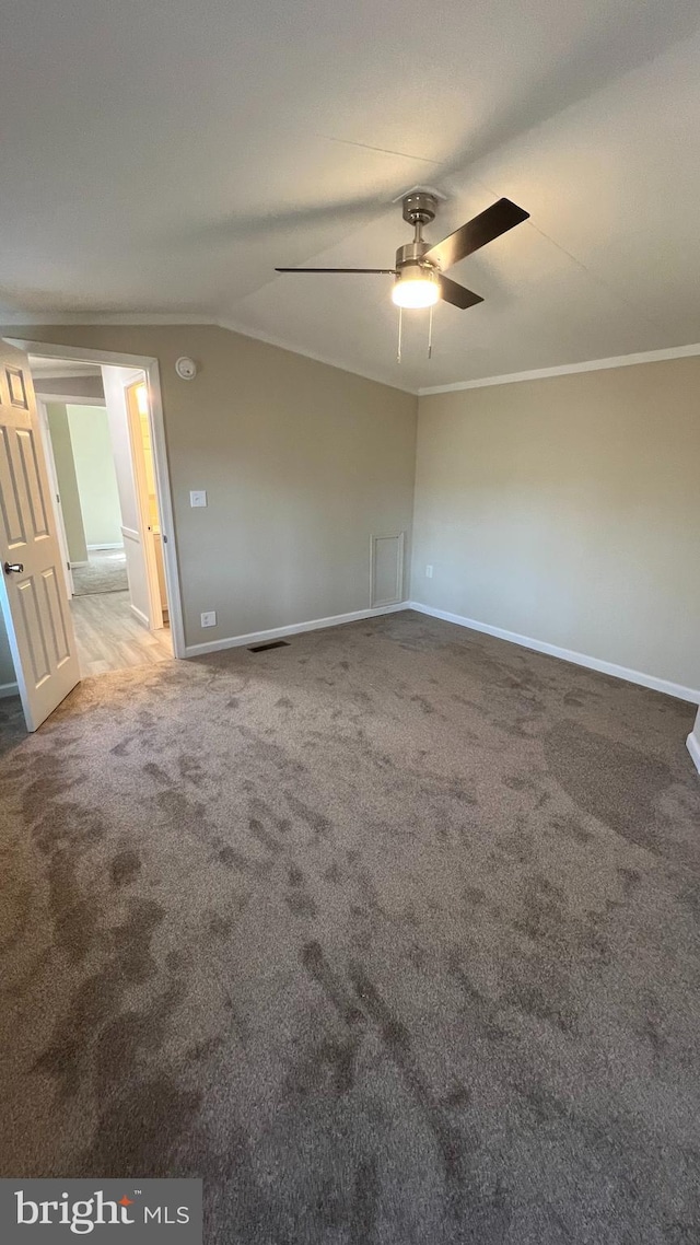 carpeted empty room featuring lofted ceiling, visible vents, ornamental molding, a ceiling fan, and baseboards