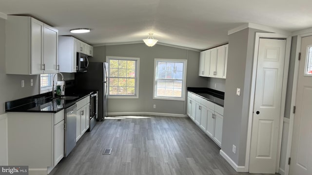 kitchen with dark countertops, white cabinetry, a sink, and stainless steel dishwasher