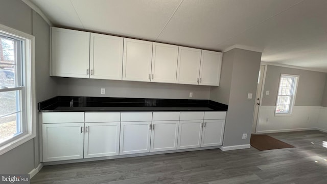 kitchen featuring a wainscoted wall, dark countertops, white cabinetry, and light wood-style floors