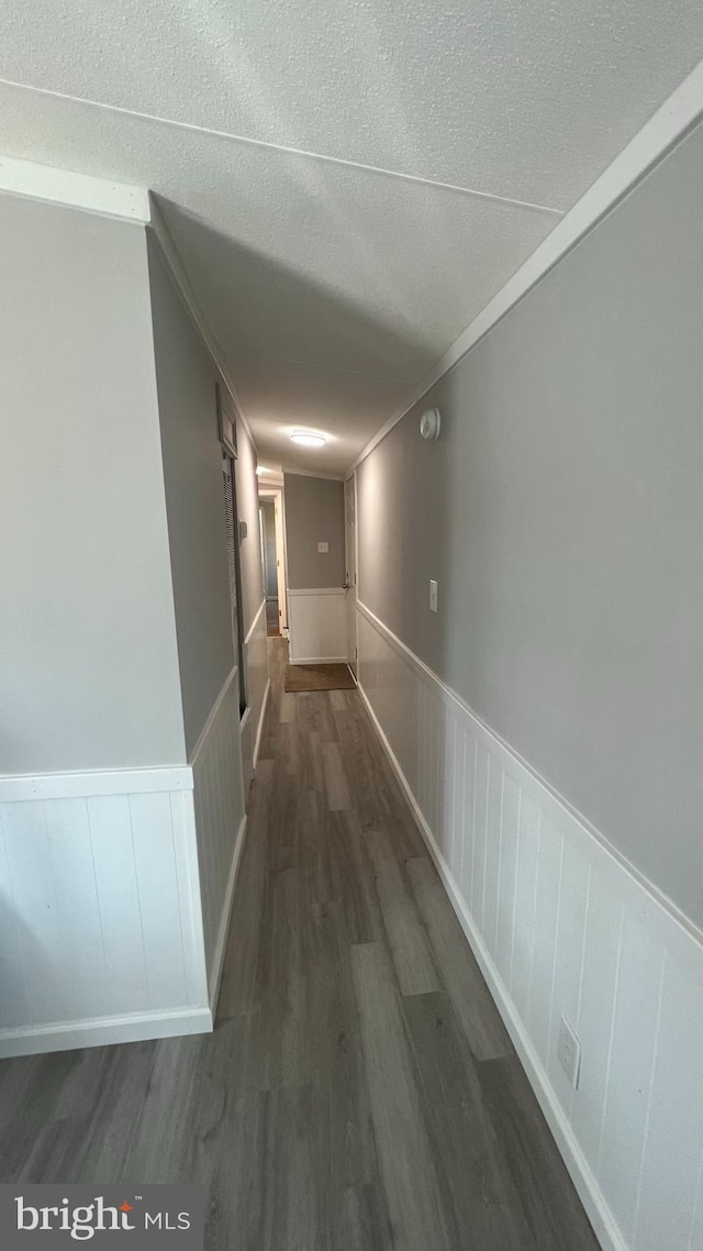 corridor with dark wood-style floors, a textured ceiling, wainscoting, and crown molding