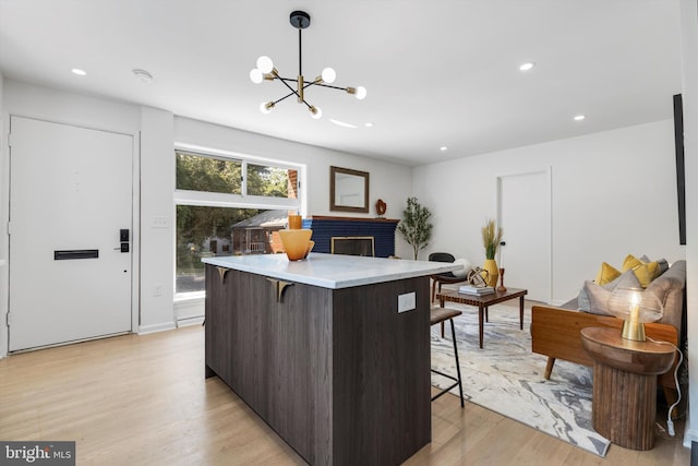 kitchen with light wood-type flooring, a brick fireplace, a breakfast bar, a notable chandelier, and hanging light fixtures