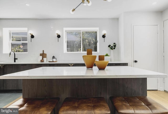 kitchen featuring decorative backsplash, dark brown cabinets, a kitchen island, and sink