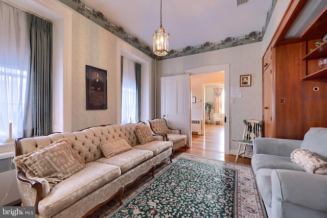 living room with hardwood / wood-style floors, radiator heating unit, a healthy amount of sunlight, and a notable chandelier