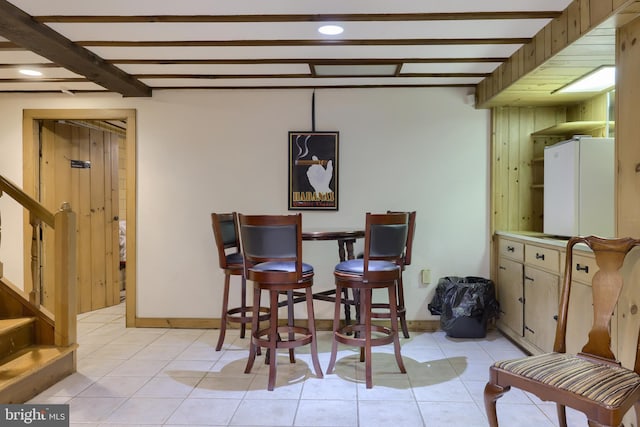 tiled dining space featuring beam ceiling