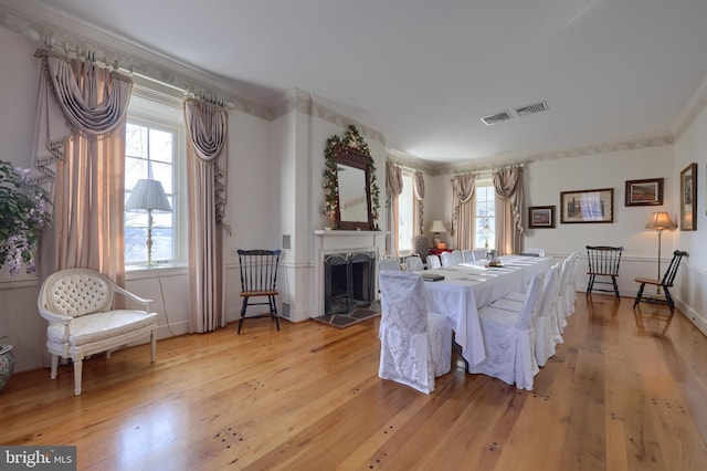 dining space with a tile fireplace, light hardwood / wood-style floors, a wealth of natural light, and crown molding