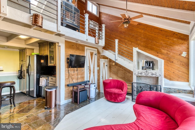 living room with a fireplace, high vaulted ceiling, ceiling fan, and wood walls