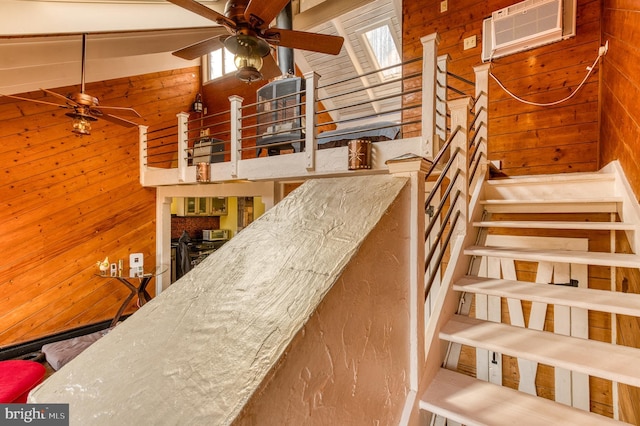 stairway featuring a wall mounted AC, vaulted ceiling with skylight, ceiling fan, and wood walls