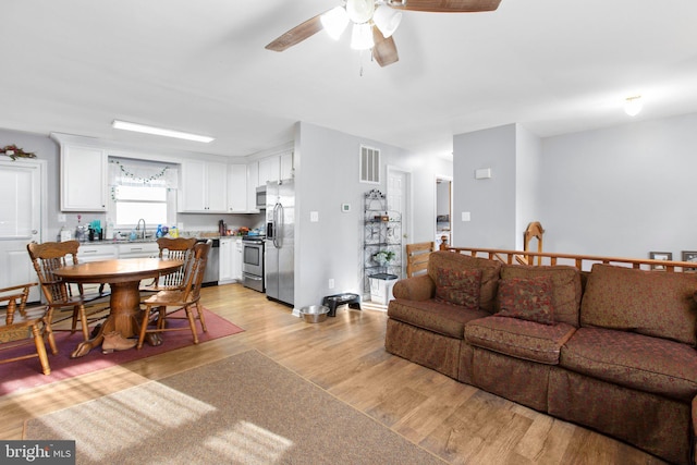 living room featuring ceiling fan, sink, and light wood-type flooring