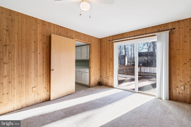 interior space featuring wood walls, ceiling fan, and light carpet