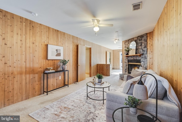 carpeted living room featuring ceiling fan, a stone fireplace, and wooden walls