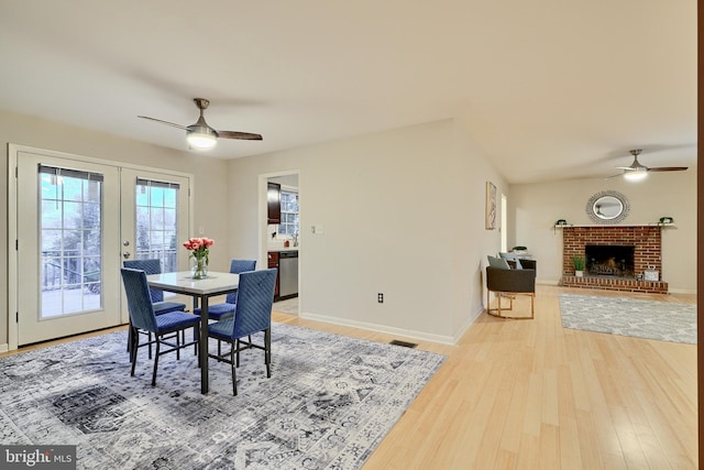 dining space with french doors, hardwood / wood-style flooring, a brick fireplace, and ceiling fan