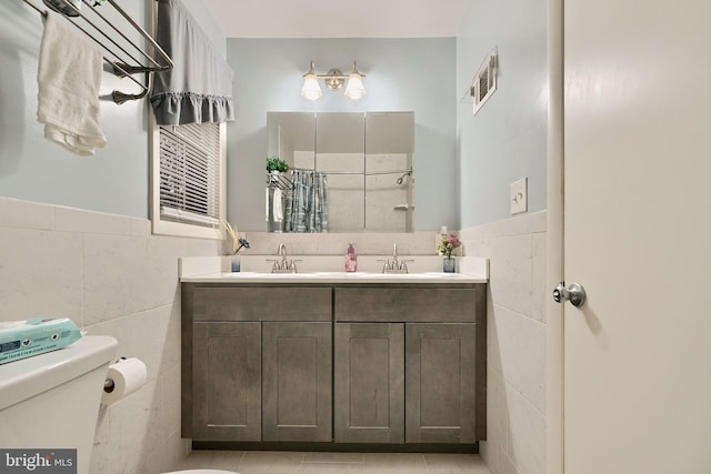 bathroom featuring tile patterned flooring, vanity, toilet, and tile walls